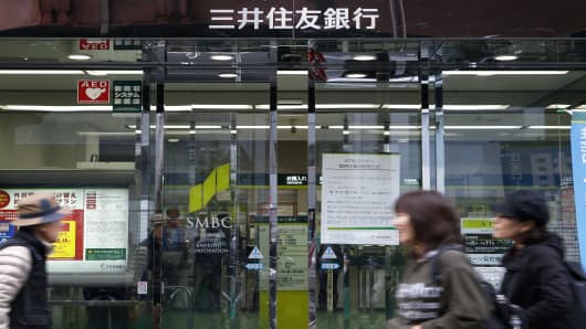 Pedestrians walk past a Sumitomo Mitsui Banking Corp. branch in Tokyo, Japan